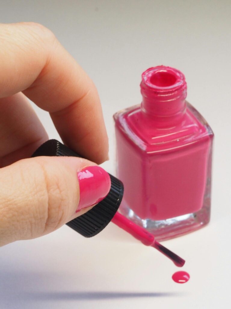 Female hand applying bright pink nail polish from open bottle, minimalistic style.